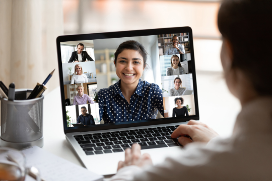 Ein Laptop mit neun Gesichtern im Videocall. Eine lächelnde Frau in der Mitte.