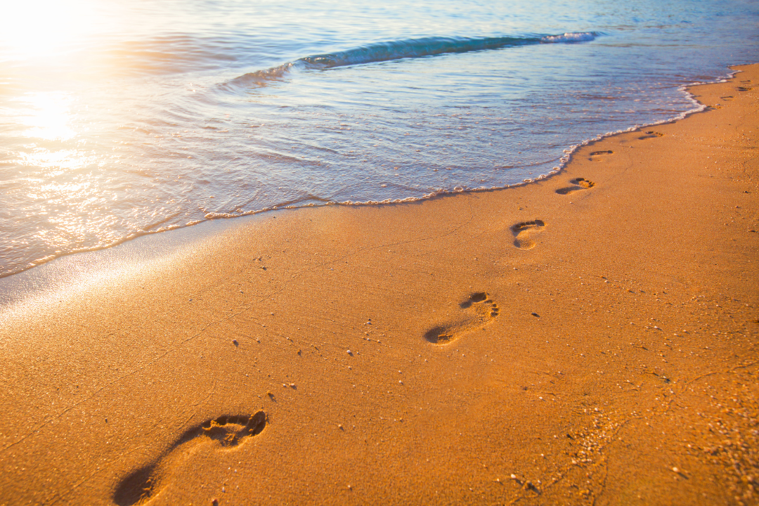 Fußspuren im Sand am Ufer, im Hintergrund die Sonne